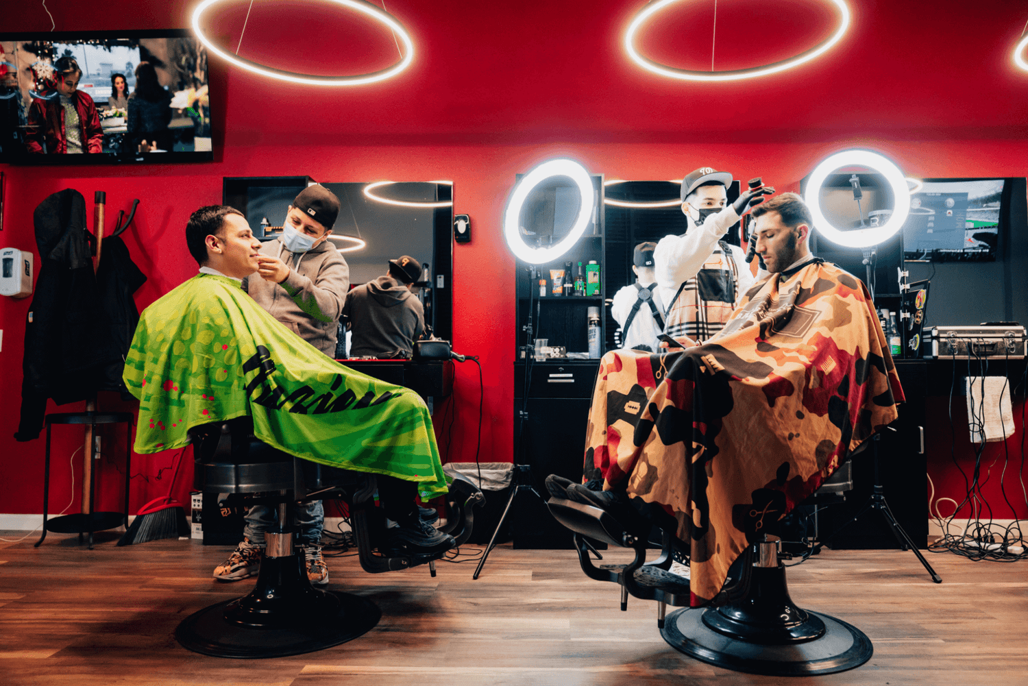 Two barbers cutting hair with white bright lights behind them.
