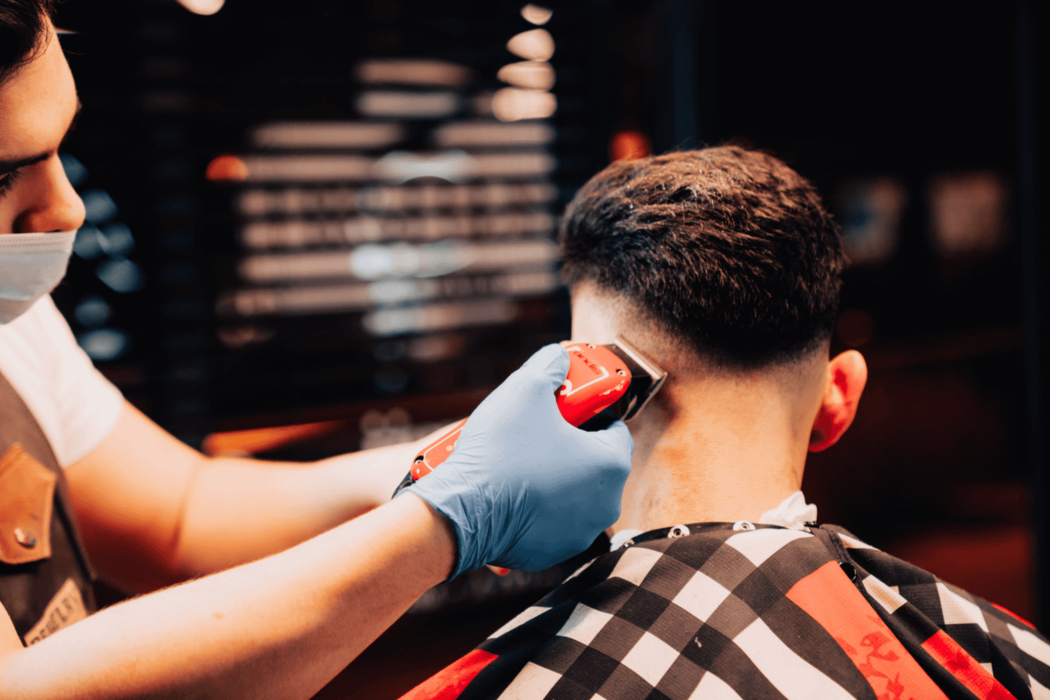 Barber cutting the side of a clients hair with red clippers.