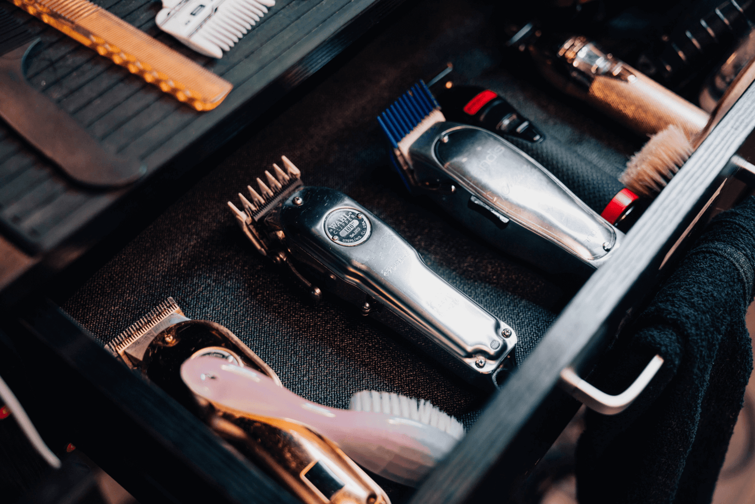 Five clippers and 2 brushes laying inside of a drawer.