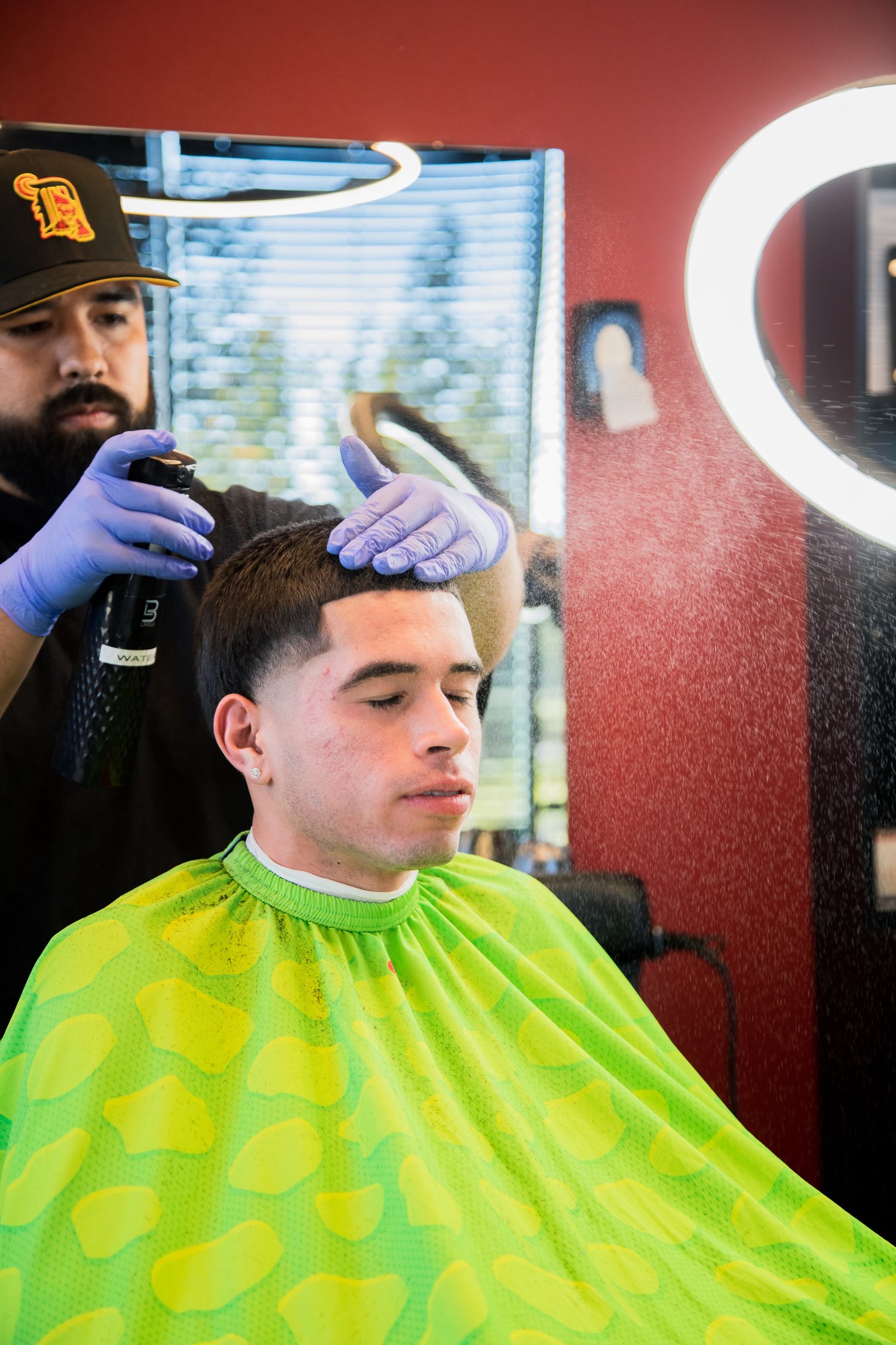 Barber in a black shirt giving a client with a green apron a haircut