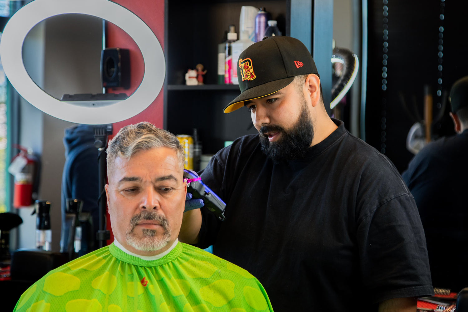 Barber in a black shirt and a black hat giving a client a haircut