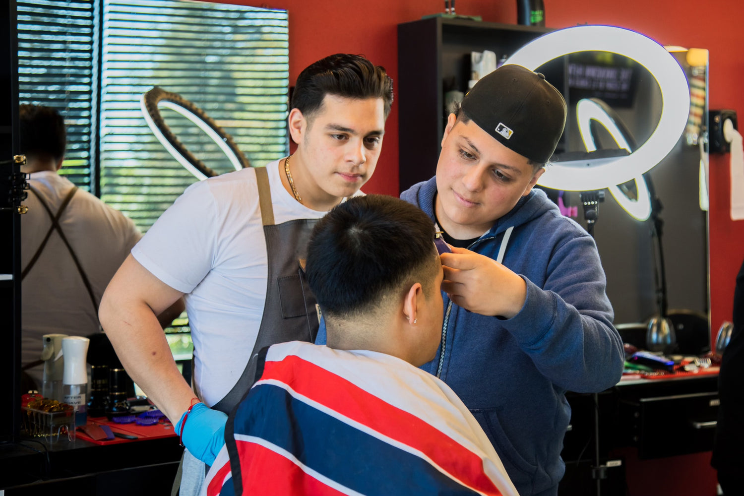 Two barbers one white shirt and one in blue sweater giving a client a haircut