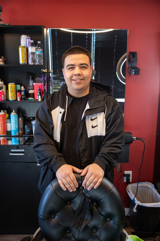 Barber in a black and white sweater leaning on black barber chair