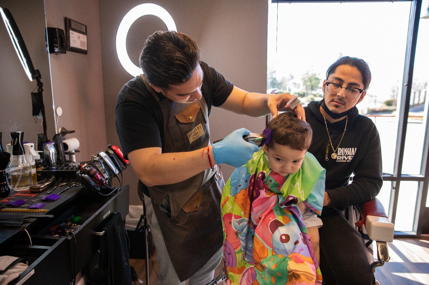 Two barbgers in black sweaters giving a child a haircut